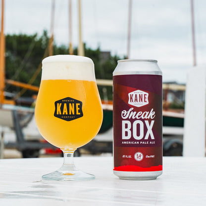 Kane Brewing Company beer glass and Sneakbox can on a table with boats in the background