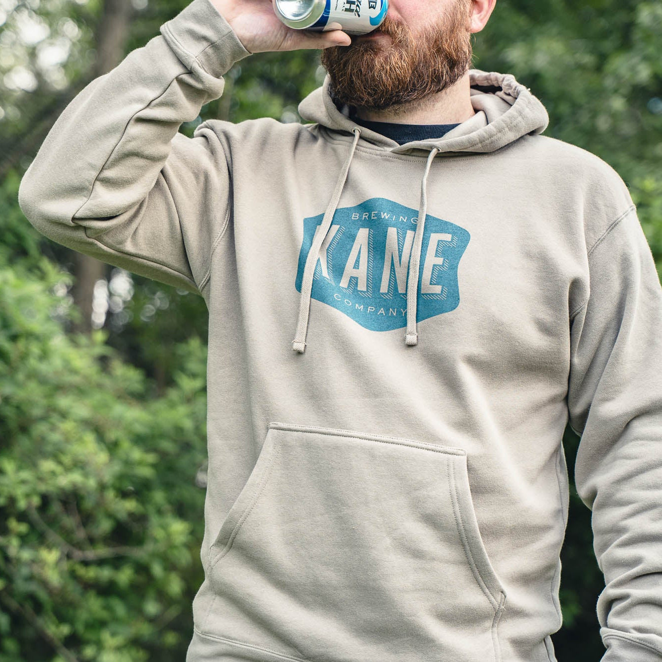 Person wearing a hoodie with Kane logo drinking Head High from a can outdoors